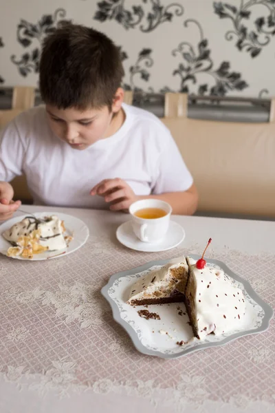 Menino bebe chá com bolo na mesa — Fotografia de Stock