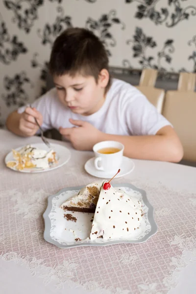 Ragazzo beve tè con torta a tavola — Foto Stock