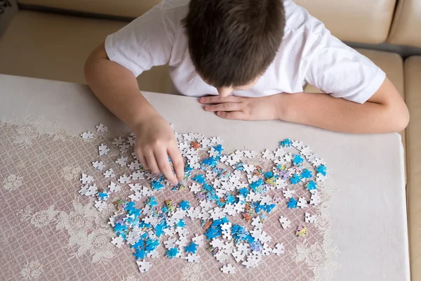 Teenager boy collects puzzles at  table — Stock Photo, Image