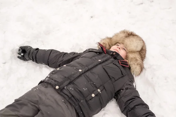 Ragazzo nel cappello invernale si trova sulla neve — Foto Stock