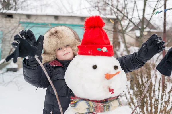 Der Junge mit der Pelzmütze um den Schneemann — Stockfoto