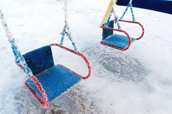 Columpio cubierto de nieve y diapositiva en el patio de recreo en invierno —  Fotos de Stock