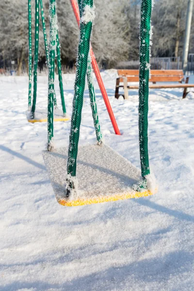 Columpio cubierto de nieve y diapositiva en el patio de recreo en invierno — Foto de Stock