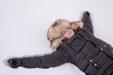 Kış şapkalı çocuk kar üzerinde yatıyor