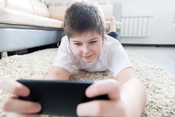 Pojke med telefonen liggande på en matta i rummet — Stockfoto