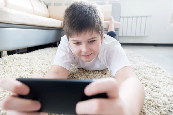 Niño con el teléfono acostado en una alfombra en la habitación — Foto de Stock