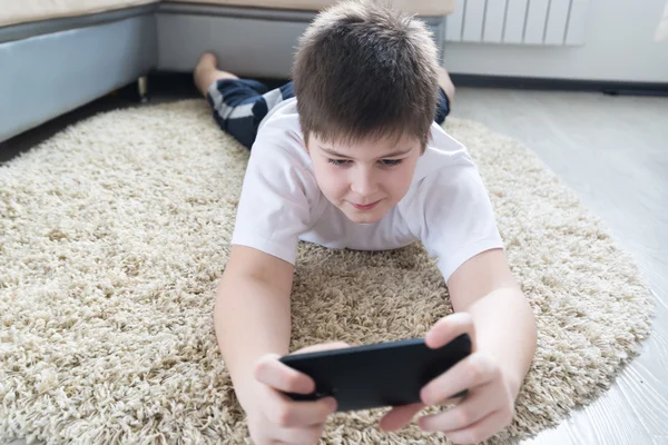 Niño con el teléfono acostado en una alfombra en la habitación — Foto de Stock