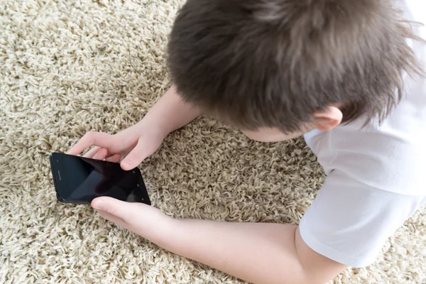 Мальчик с телефоном лежит на ковре в комнате — стоковое фото