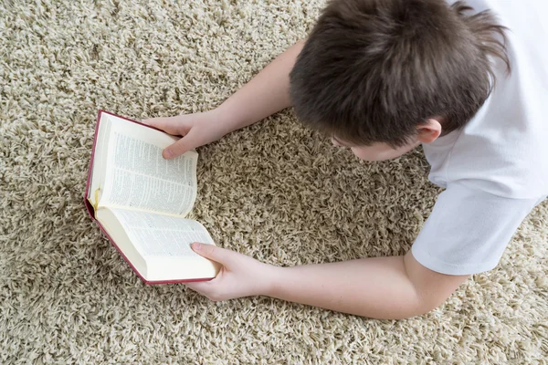 Ragazzo che legge un libro mentre giace su un tappeto nella stanza — Foto Stock