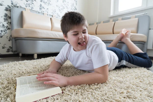 Chłopiec czytając książkę leżąc na dywanie w pokoju — Zdjęcie stockowe