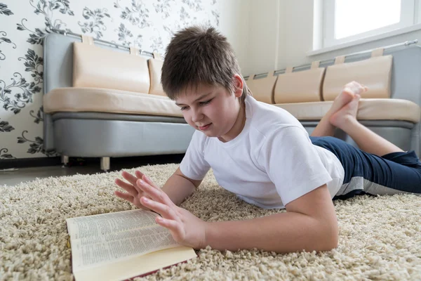 Chłopiec czytając książkę leżąc na dywanie w pokoju — Zdjęcie stockowe