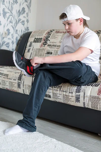 Der Junge trägt Laufschuhe, sitzt auf einem Sofa im Zimmer — Stockfoto