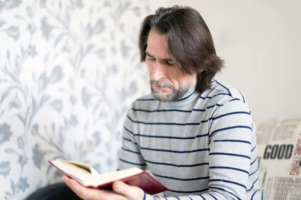 Homem barbudo lendo um livro na sala de estar — Fotografia de Stock