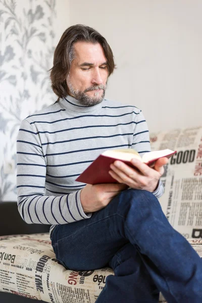 Homem barbudo lendo um livro na sala de estar — Fotografia de Stock