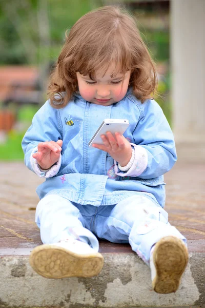 Flicka två år, med en mobiltelefon i parken — Stockfoto