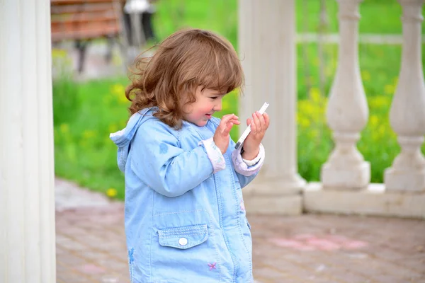 Flicka två år, med en mobiltelefon i parken — Stockfoto