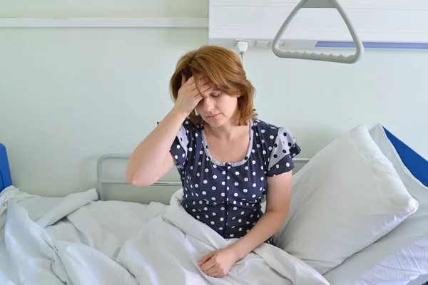 Female patient with headache on bed in hospital ward — Stock Photo, Image