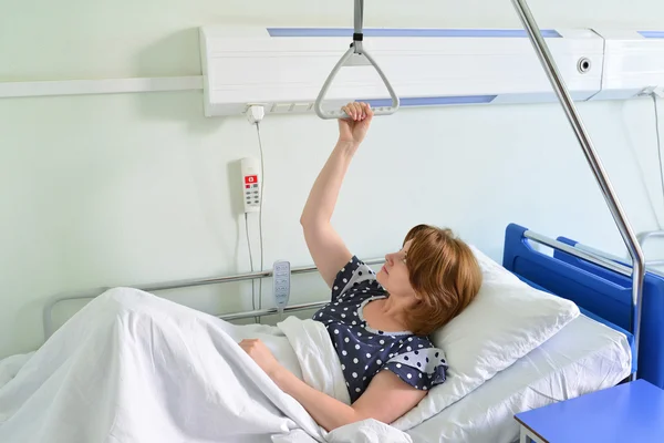 Paciente femenina aferrada al dispositivo de elevación en la habitación del hospital Fotos de stock libres de derechos