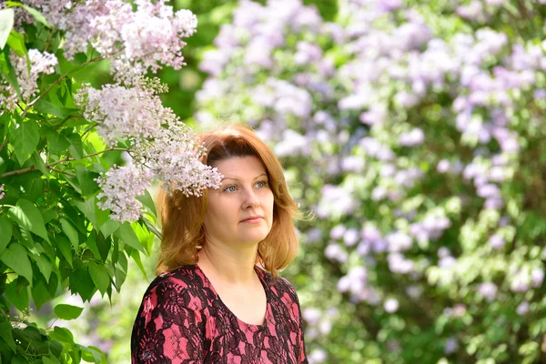 Mulher de meia-idade perto de florescer lilás — Fotografia de Stock