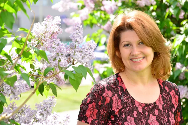 Middelbare leeftijd vrouw in de buurt van bloeiende lila — Stockfoto