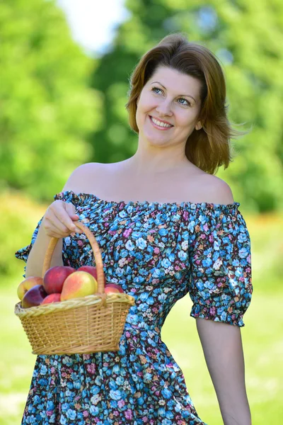 Volwassen vrouw met een mand fruit in het park — Stockfoto