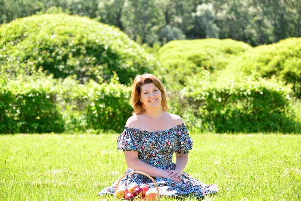 Volwassen vrouw met een mand fruit in het park — Stockfoto