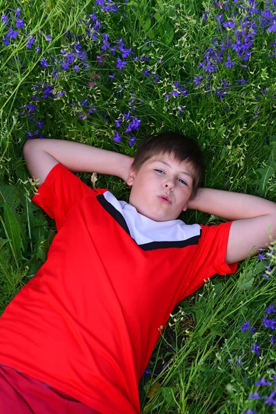 Menino adolescente descansando no gramado com flores azuis — Fotografia de Stock