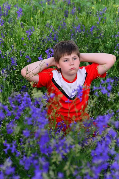 Menino adolescente descansando no gramado com flores azuis — Fotografia de Stock