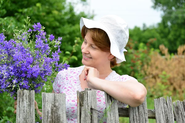 Donna con fiori di campo vicino alla recinzione in legno nel villaggio — Foto Stock