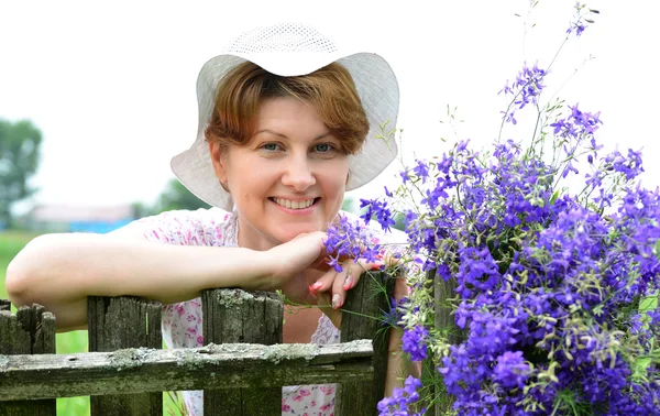 Donna con fiori di campo vicino alla recinzione in legno nel villaggio — Foto Stock