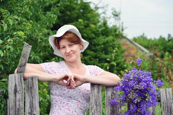 Donna con fiori di campo vicino alla recinzione in legno nel villaggio — Foto Stock