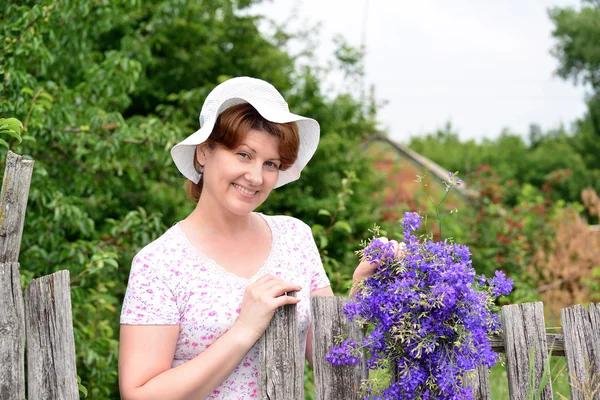 Donna con fiori di campo vicino alla recinzione in legno nel villaggio — Foto Stock