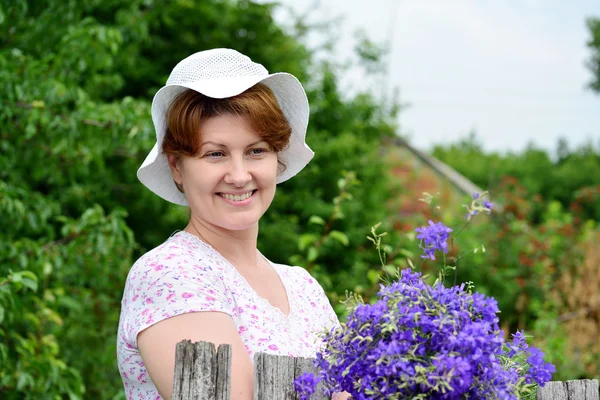 Vrouw met wilde bloemen in de buurt van houten hek in het dorp — Stockfoto