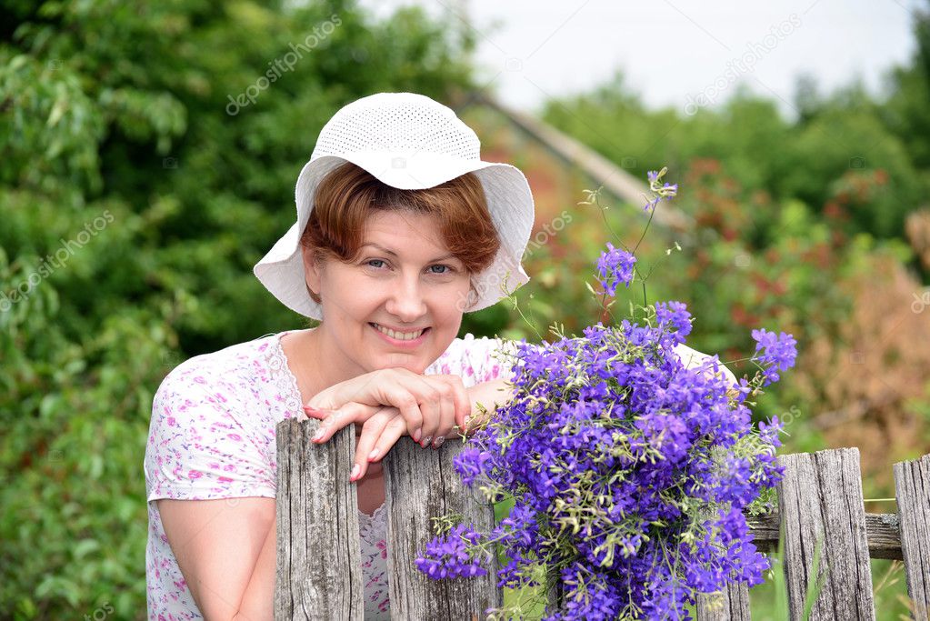 Woman with   wildflowers near  wooden fence in the village
