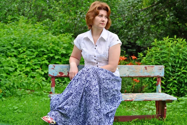 Взрослая женщина сидит на скамейке в саду — стоковое фото