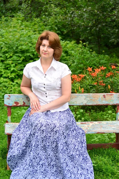 Adult woman sitting on a bench in the garden — Stock Photo, Image