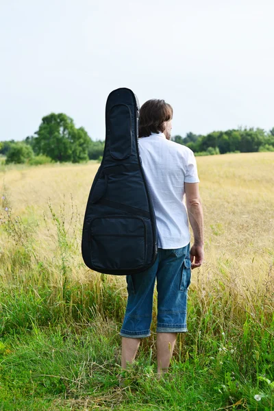 A man with a guitar in a field — Stock Photo, Image