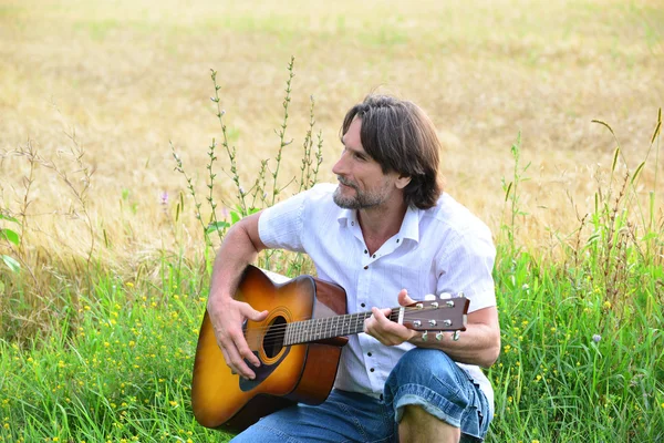 Un hombre con una guitarra en un campo — Foto de Stock