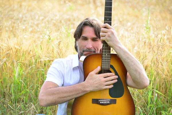 A man with a guitar in a field — Stock Photo, Image