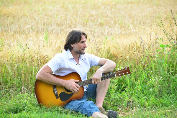 A man with a guitar in a field — Stock Photo, Image