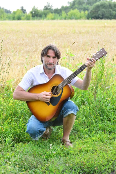 A man with a guitar in a field — Stock Photo, Image