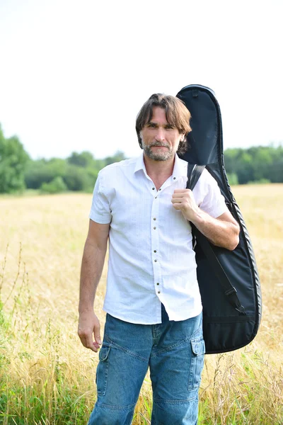 A man with a guitar in a field — Stock Photo, Image