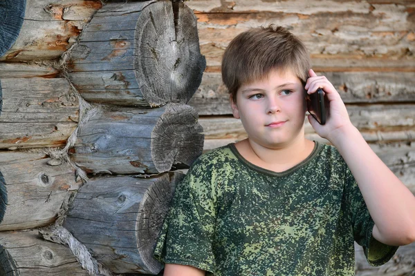 किशोर लड़का लकड़ी की दीवार के पास खड़े सेल फोन पर बात कर रहा है — स्टॉक फ़ोटो, इमेज