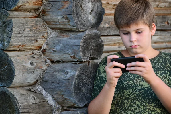 Boy teenager writes sms standing by awooden wall — Stock Photo, Image