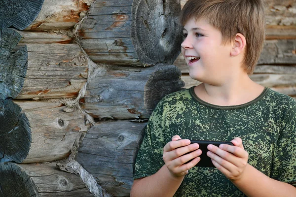 Boy teenager writes sms standing by awooden wall — Stock Photo, Image