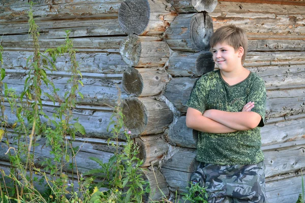 Adolescente menino em camuflagem fica perto de parede de madeira — Fotografia de Stock