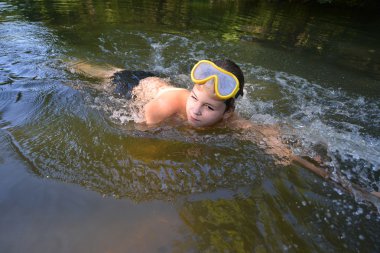 Çocuk genç nehirde yazında yüzer.