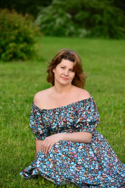 Woman in a dress with open shoulders sitting on the grass — Stock Photo, Image