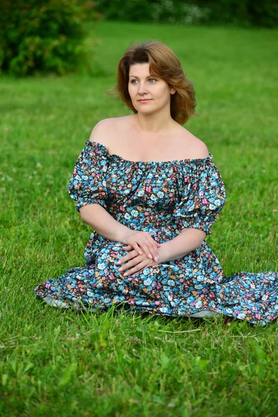Женщина в платье с открытыми плечами сидит на траве — стоковое фото