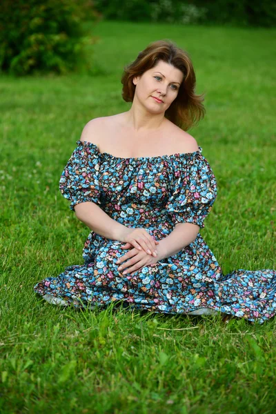 Woman in a dress with open shoulders sitting on the grass — Stock Photo, Image